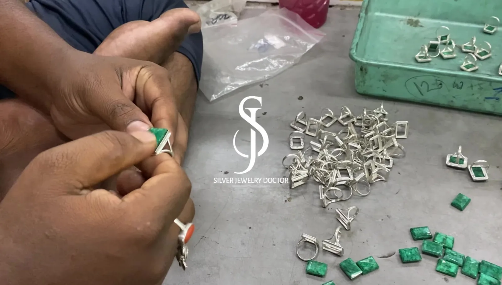 Green gemstones being set into sterling silver jewellery components by hand